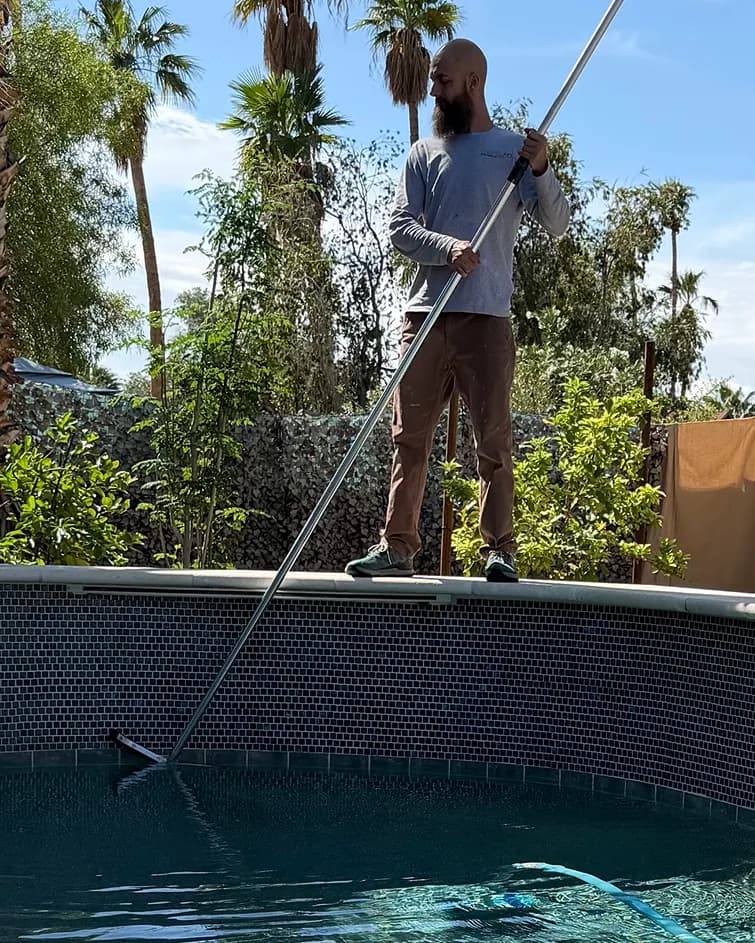 Technician cleaning pool wall with brush pole in North Phoenix