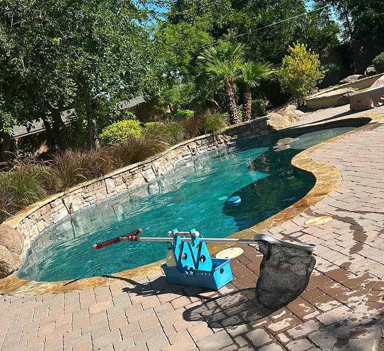 Skimmer net and tool caddy on deck beside cleaned pool